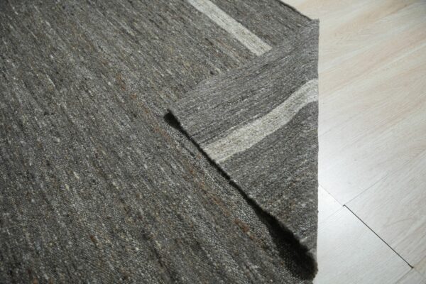 Speckled gray rug folded back revealing light cream and brown stripes on pale plank flooring.