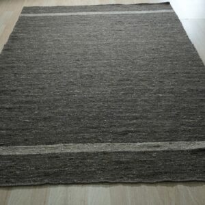 A dark gray textured area rug with two light horizontal stripes lies on light wood flooring.