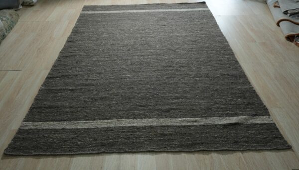 A dark gray textured area rug with two light horizontal stripes lies on light wood flooring.