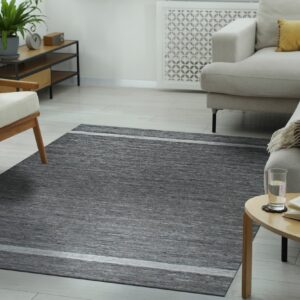 Gray striated area rug centered between a beige sectional sofa and a light wood armchair on pale flooring.