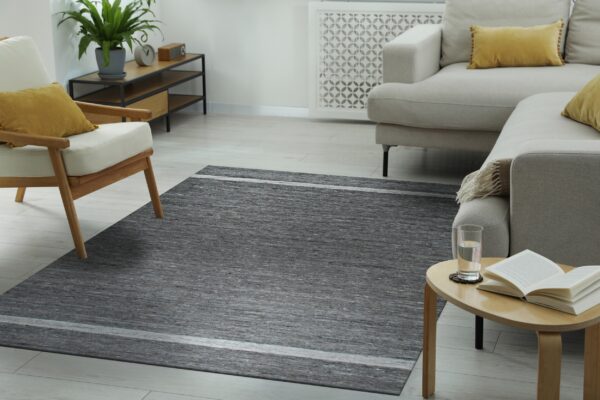 Gray striated area rug centered between a beige sectional sofa and a light wood armchair on pale flooring.