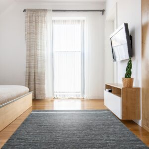 Dark gray heathered rug with a single light stripe anchors a bright room with wooden furniture and sheer curtains.