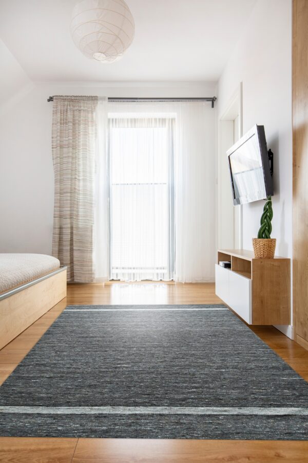 Dark gray heathered rug with a single light stripe anchors a bright room with wooden furniture and sheer curtains.