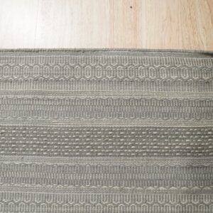 Textured gray flatweave rug with striped, loop, and dotted patterns rests on light blonde wood flooring.