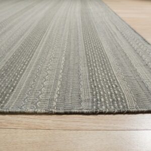 Gray low-pile rug featuring alternating textured vertical stripe patterns rests on light wood flooring.