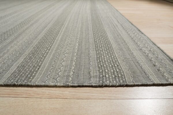 Gray low-pile rug featuring alternating textured vertical stripe patterns rests on light wood flooring.