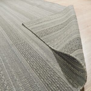 Close-up of a gray flatweave rug featuring textured stripes, partially rolled on light blonde wood flooring.