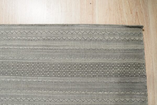 A gray flat-woven rug with light geometric stripe patterns rests on light wood plank flooring.