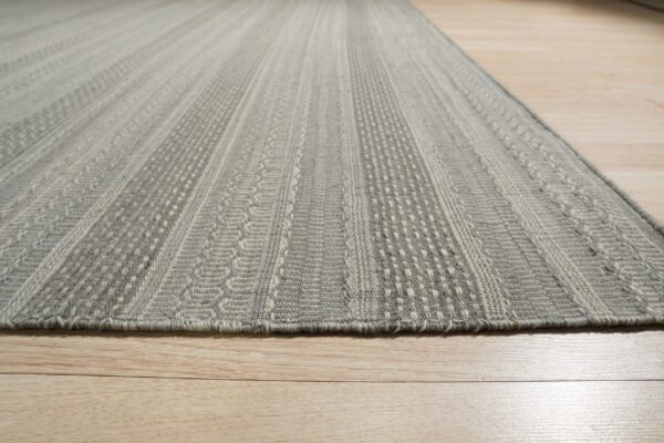 Low angle view of a gray textured flatweave rug with vertical patterned bands on light flooring.