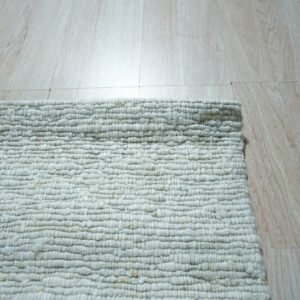 Close-up of a chunky, textured off-white looped rug corner resting on light blonde wood plank flooring.