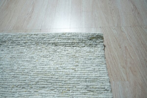Close-up of a chunky, textured off-white looped rug corner resting on light blonde wood plank flooring.