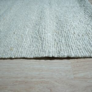 Close-up of a chunky, off-white loop-textured rug resting on light blonde wood plank flooring.