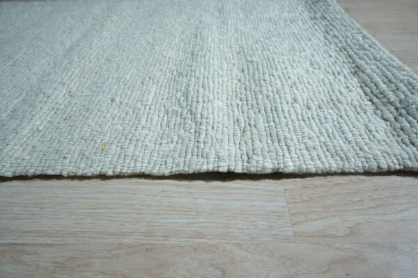 Close-up of a chunky, off-white loop-textured rug resting on light blonde wood plank flooring.