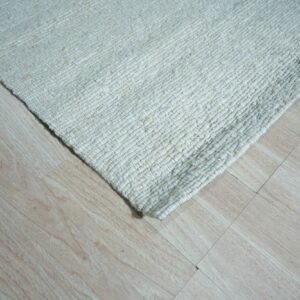 Chunky woven off-white rug corner resting on light blonde wood grain flooring.