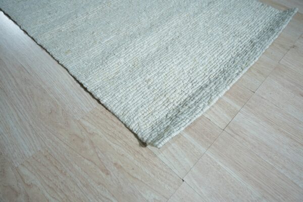 Chunky woven off-white rug corner resting on light blonde wood grain flooring.