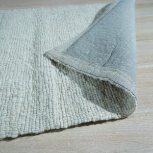 Close up of a cream chunky looped rug with a grey fabric backing shown on light wood floor.