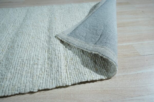 Close up of a cream chunky looped rug with a grey fabric backing shown on light wood floor.