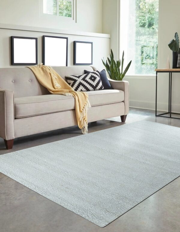 Light gray subtly striped rug anchors a living area with a neutral sofa and large sunlit windows.