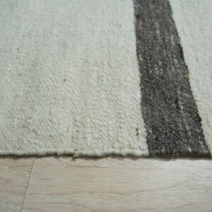 Chunky textured rug in cream and dark gray stripes, shown closely on light wood flooring.