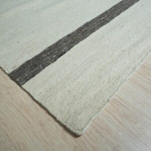 A low-pile natural white rug with a thick charcoal stripe sits on light wood plank flooring.