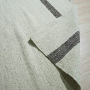 Coarse off-white rug with thick dark brown stripes, partially folded on light wood flooring.