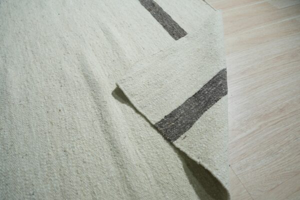 Coarse off-white rug with thick dark brown stripes, partially folded on light wood flooring.