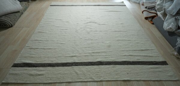 Textured off-white rug with contrasting dark gray horizontal stripes lying on a light plank floor.