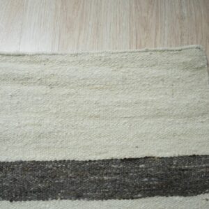 Low-pile striped rug in off-white and charcoal gray resting on light blonde hardwood flooring.