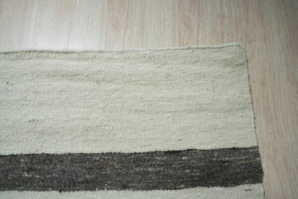 Low-pile striped rug in off-white and charcoal gray resting on light blonde hardwood flooring.