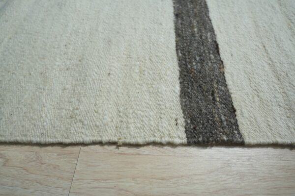 Off-white textured rug featuring a heathered dark gray stripe resting on light blonde wood flooring.