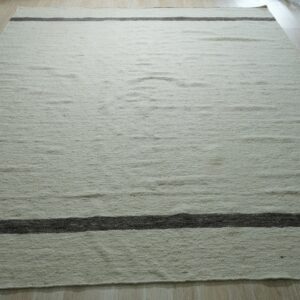Textured cream rug with two dark brown horizontal stripes resting on light wood plank flooring.
