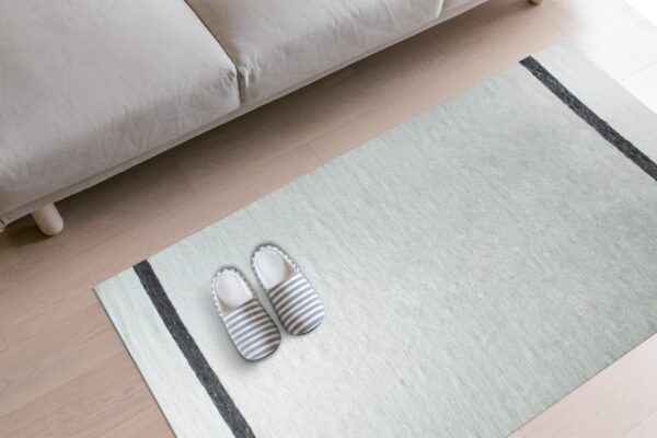 Light blue rug with charcoal stripes sits beneath a light beige couch on wood flooring.