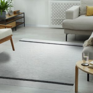 Flatweave gray rug with black stripes grounding a modern living space with beige furniture and light wood floors.