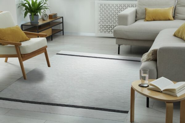 Flatweave gray rug with black stripes grounding a modern living space with beige furniture and light wood floors.