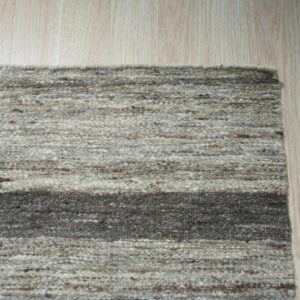 Variegated gray and brown striped rug with chunky texture lying on pale blonde wood flooring.