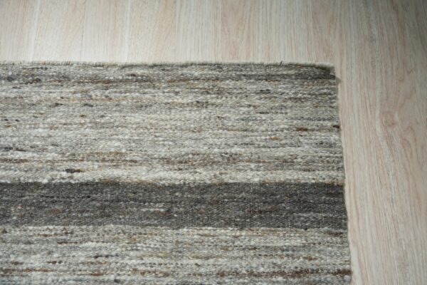 Variegated gray and brown striped rug with chunky texture lying on pale blonde wood flooring.