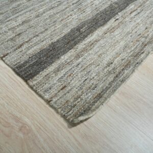 Textured gray and brown striped rug corner with a thick dark stripe rests on light blonde wood floorboards.