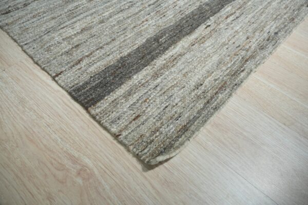 Textured gray and brown striped rug corner with a thick dark stripe rests on light blonde wood floorboards.