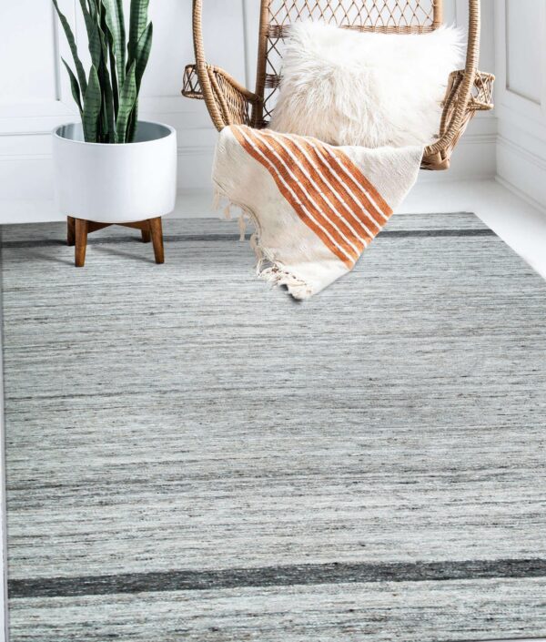 Textured light gray rug featuring a dark stripe, placed on a white floor near a potted plant and wicker chair.