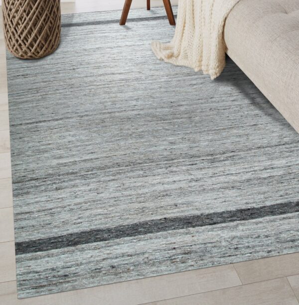 The textured gray area rug with horizontal striations and a dark band lies beneath a beige couch.