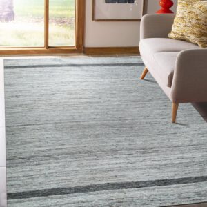 A textured gray rug with horizontal dark stripes covers the floor next to a light beige sofa and large window.
