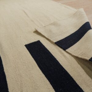 Flatweave rug in beige, navy, and gold geometric stripes folded on light wood floor.