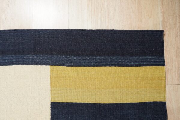 Flatweave rug with blocks of navy blue, gold, and cream on light wood plank flooring.