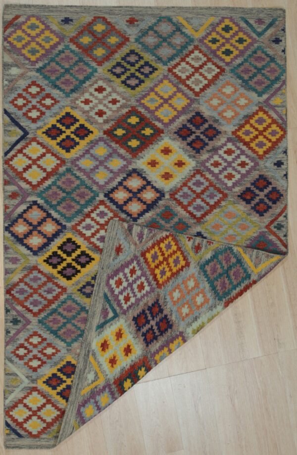 Geometric rug with multicolored diamond patterns on a muted gray ground, shown folded on light wooden floorboards.