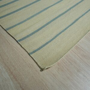 Close-up of a cream flatweave rug with thin blue stripes resting on light wood flooring.