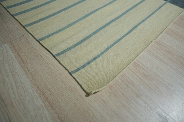 Close-up of a cream flatweave rug with thin blue stripes resting on light wood flooring.