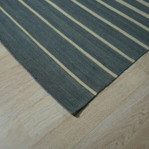 Flatweave rug in dark gray with light stripes sits on pale wood plank flooring.