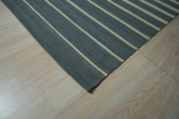 Flatweave rug in dark gray with light stripes sits on pale wood plank flooring.