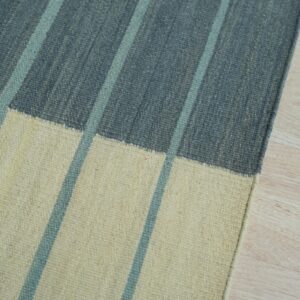 Low-pile rug with vertical blue stripes on slate gray and cream blocks over light wood flooring.