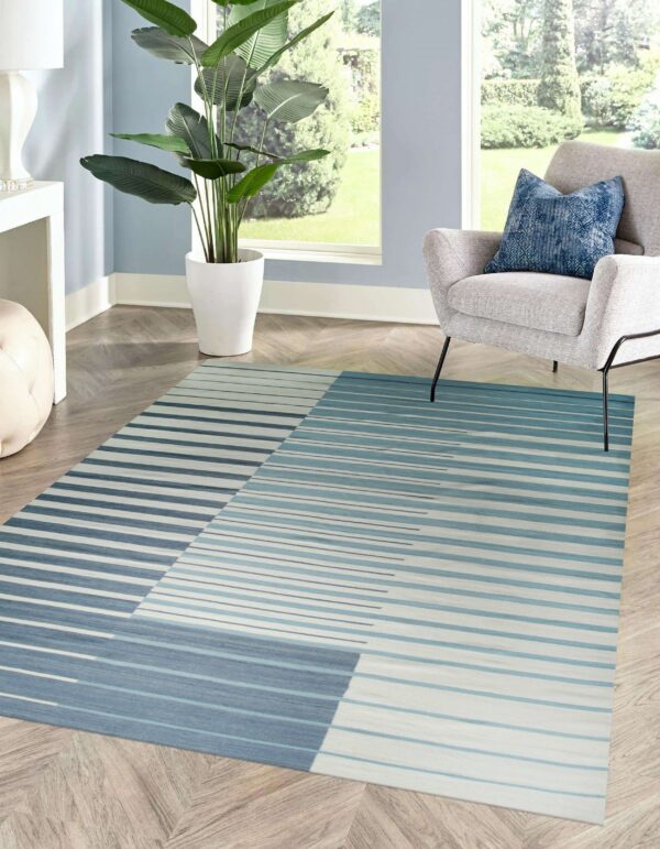 Diagonal color-blocked rug with fading horizontal blue and white stripes on herringbone wood flooring.